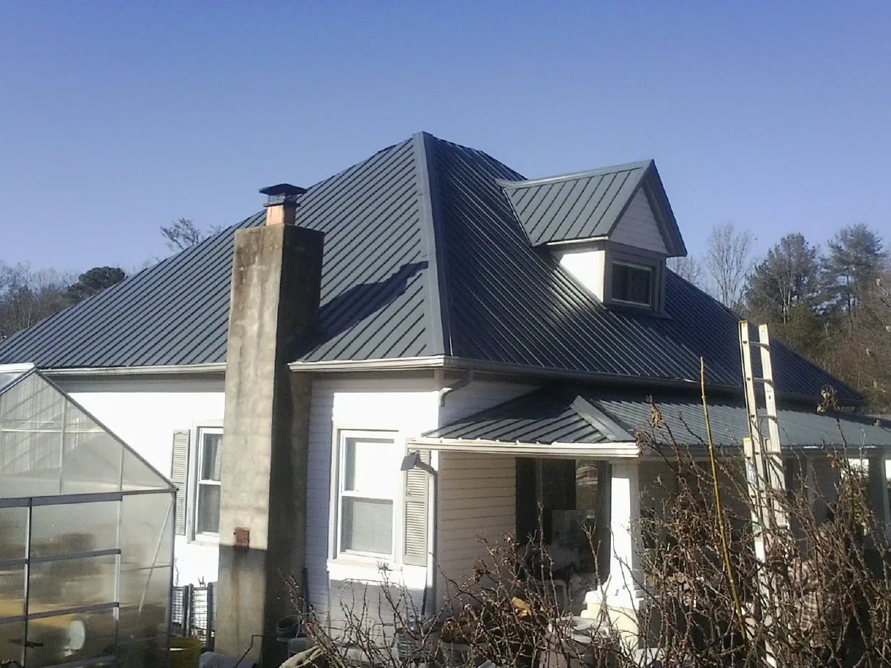 Dark blue standing seam metal roof on a white farmhouse with dormer — Slate & Tile Roof Repair by Roofing Brothers in Mc Alisterville
