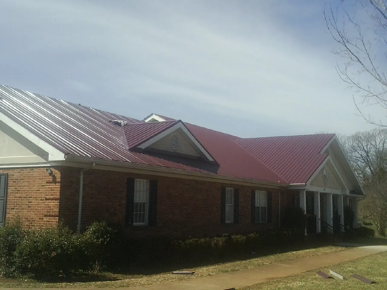 Red metal roof with gabled entries on a long brick building, from a Hail Damage Roof Repair job in Mc Alisterville