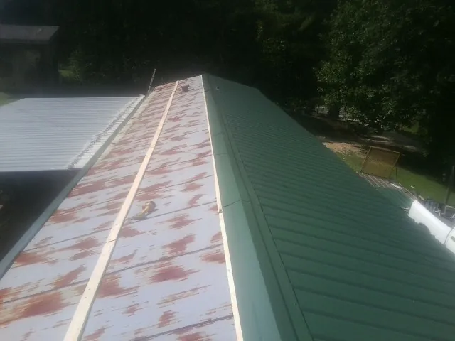 Old rusted panels beside newly installed green metal roofing — Wind Damage Roof Repair by Roofing Brothers in Mc Alisterville
