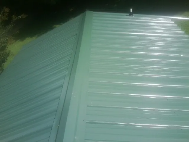 New green metal panels meeting at the ridge of a roof — Flat Roof Repair work by our crew in Mc Alisterville