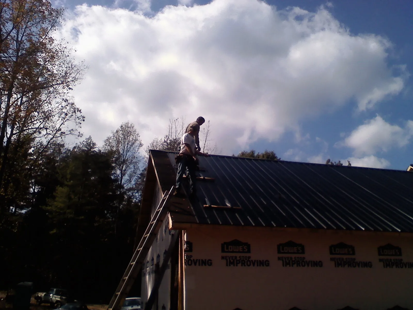 Roofer fastening dark metal panels high against a cloudy sky, from a Roof Inspection job in Mc Alisterville