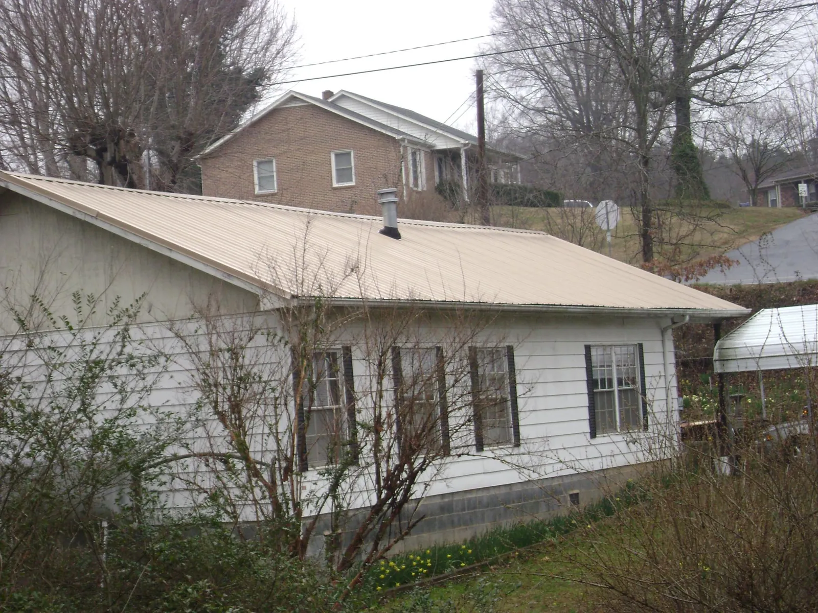 Tan metal roof on a white sided house set into a hillside — Commercial Roofing by Roofing Brothers in Mc Alisterville